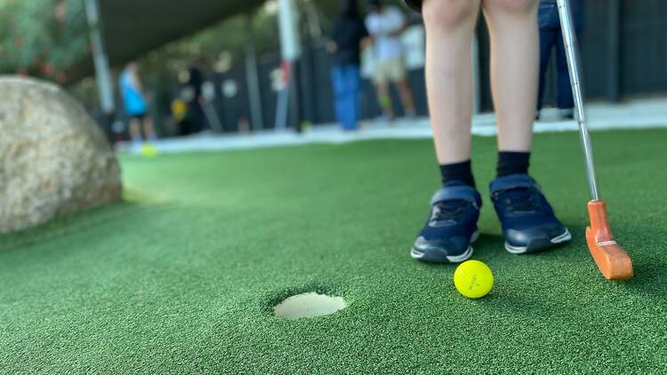 Close up of a gold ball and putter at a mini golf course