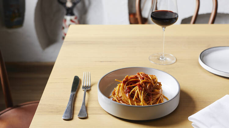A dish of spaghetti atop a wooden table, with a glass of red wine.