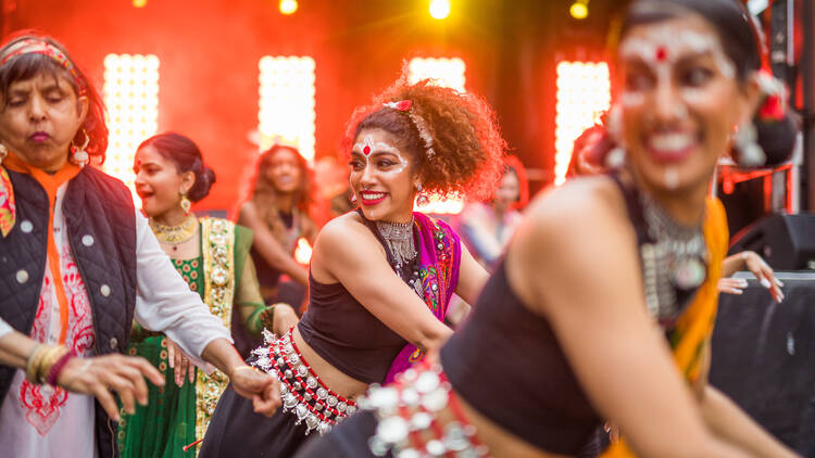 A group of women dressed in saris dance in formation.