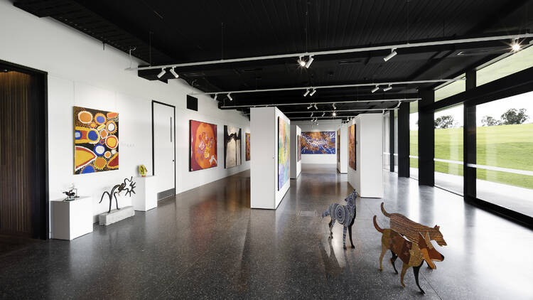 A gallery with white walls houses Indigenous art. Three dog sculptures sit in the foreground.