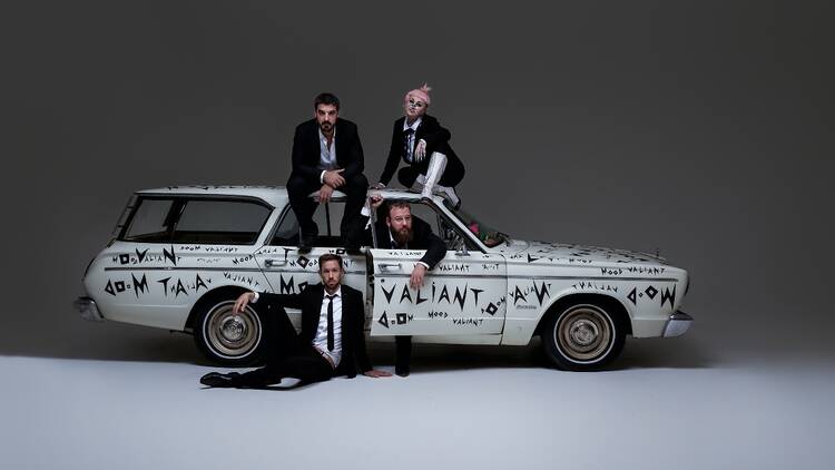 Four band members posed with a white graffitied car