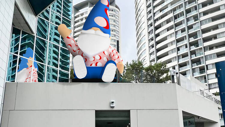 A giant digital gnome waves from the top of a building.