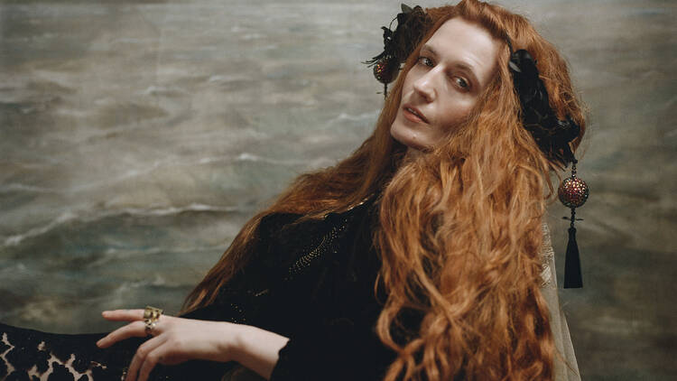 Florence and the Machine singer Florence Welch reclines on a chair dressed in a velvet robe, her red hair flowing down the side of the chair