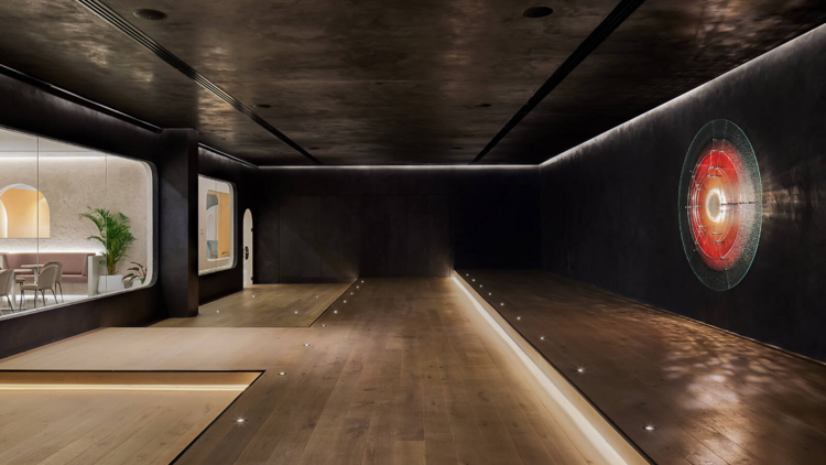 A futuristic, low lit pilates studio with timber floors and an illuminated red circle on the black wall