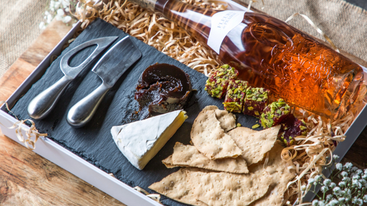 A cheese board with crackers, brie cheese, turkish delight and a bottle of. pink coloured liqueur 