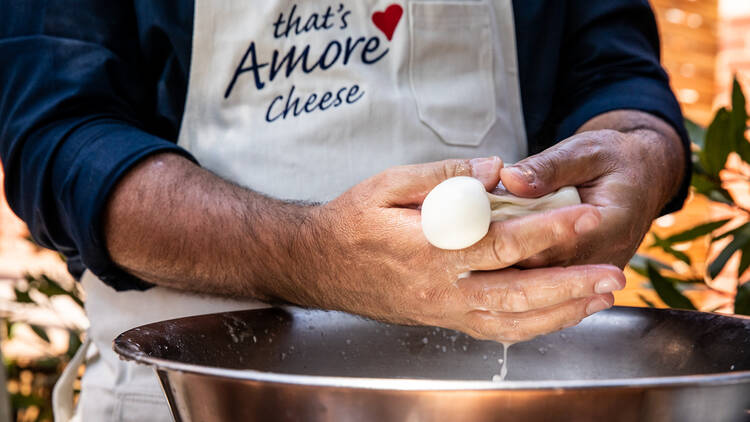 A man making cheese in a metal bowl.