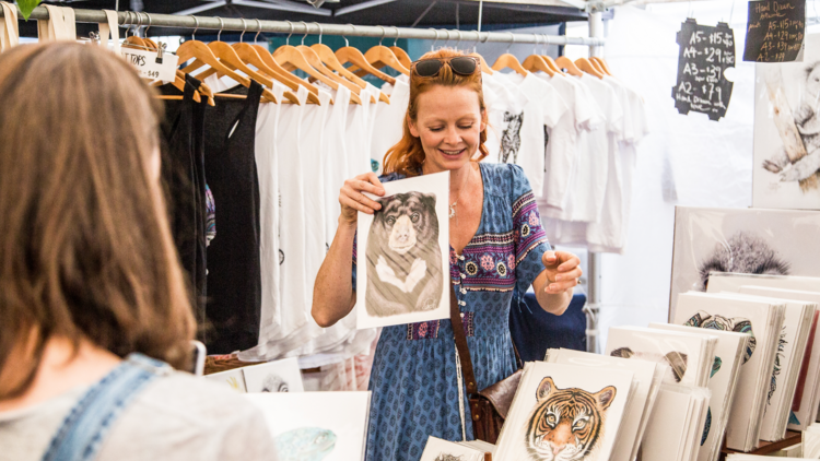 A woman holds up a printed picture in a market stall