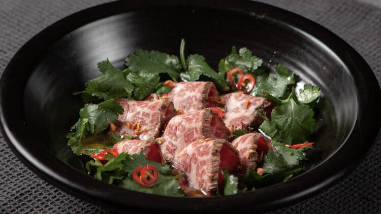 A bowl of wagyu tataki surrounded by cilantro and chilis.