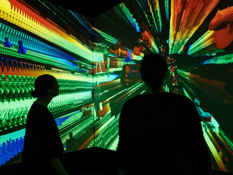 Two people stand in front of a video installation showing a rainbow of colours