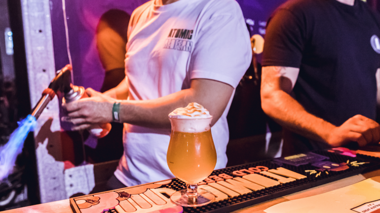 A beer with a freshly torched meringue on top of it sits on a bar 