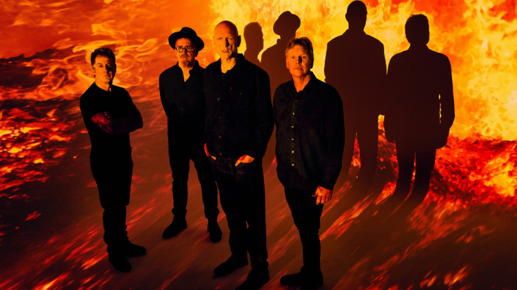 Midnight Oil pose in front of a red and yellow backdrop resembling flames