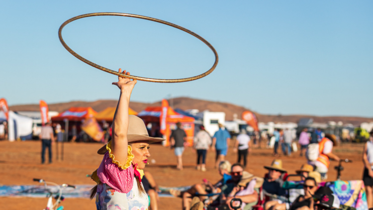 Photograph of the a woman holding a whirling hoola hoop above her head at the Mundi Mundi desert festival 