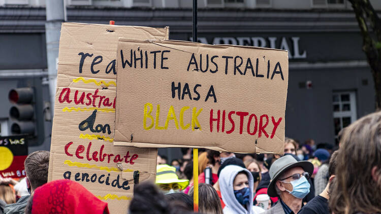 Protesters holding signs reading 'white australia has a black history'. 