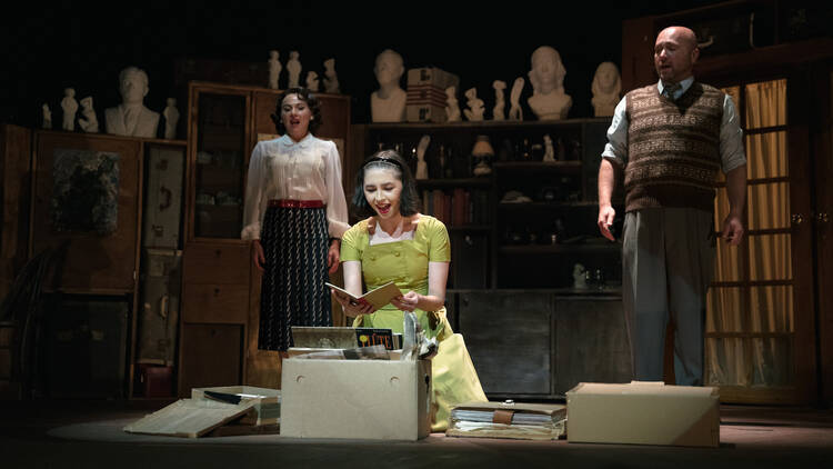 A young girl in green looks fascinated as she peers at an open book, her parents standing behind her