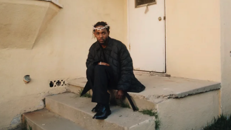 Kendrick Lamar wearing a thorned crown while sitting on outdoor stairs.