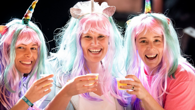 Three people in unicorn wigs pose with plastic cups full of beer