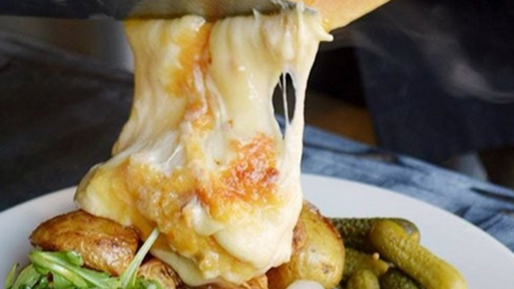 A piece of thick melted cheese is spooned over potatoes and salad 