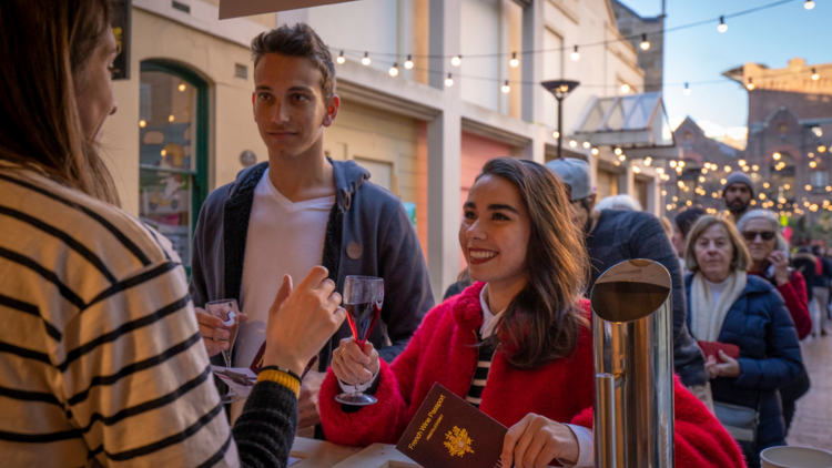 Two people holding a French passport smile at a wine stall 