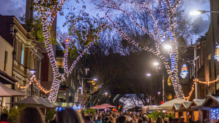 A shot of the crowd gathered at the Rocks at night, for a street festival, everything illuminated by two big trees wrapped in fairy lights