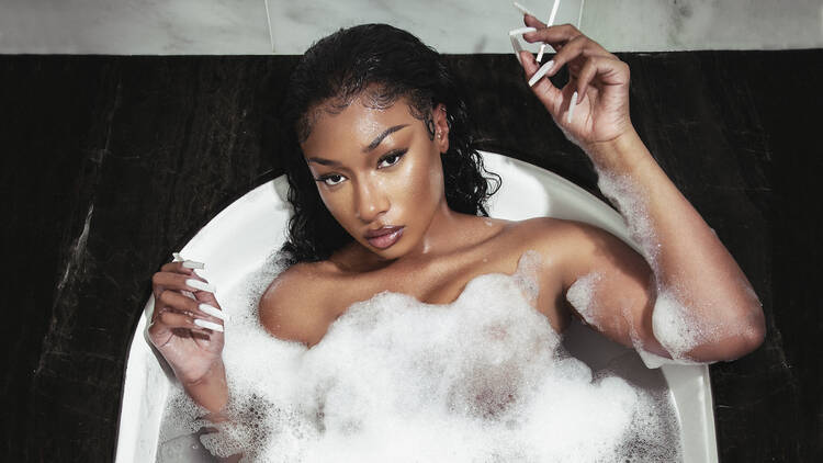 Megan Thee Stallion sits in a bubble bath, looking at the camera, a cigarette in hand