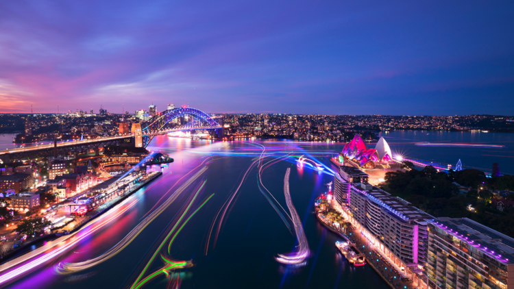 An aerial shot of Sydney Harbour at dusk lit up with lights from Vivid.