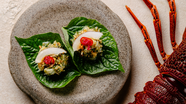 An entree served on betel leaf upon a stone platter, with a lobster visible in the background.