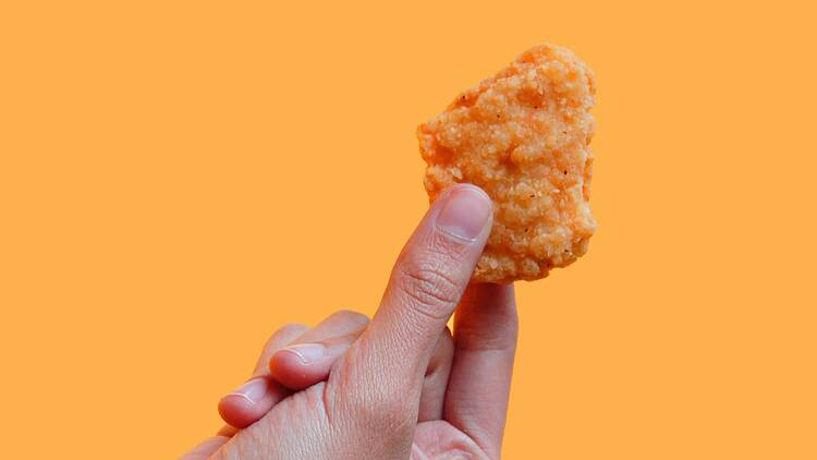 A hand holding one chicken nugget