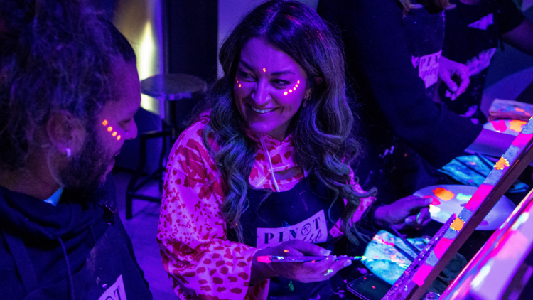 A woman laughs with neon paint on her face 