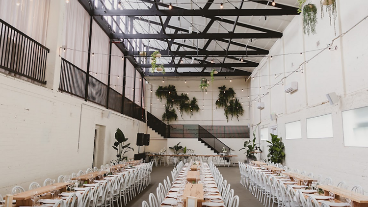 The interoir of a warehouse venue with long tables and wedding decor.