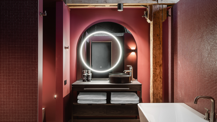 A pink-tiled bathroom with a tub and circular mirror.