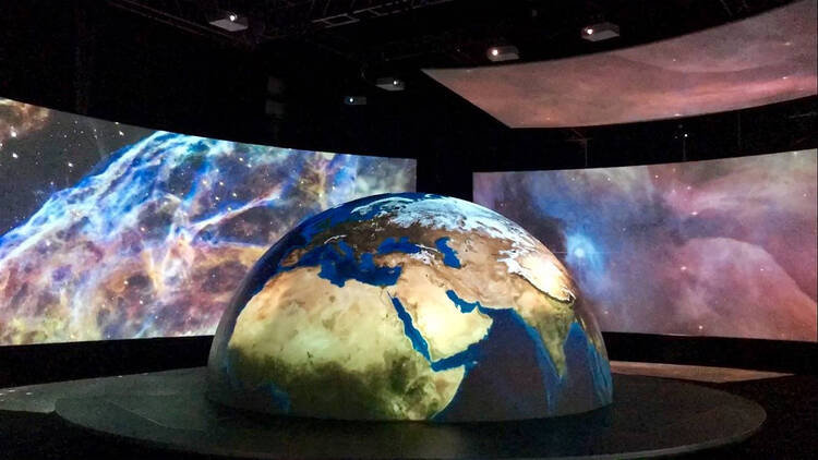 A model of Earth in a room illuminated by screens with galaxies.