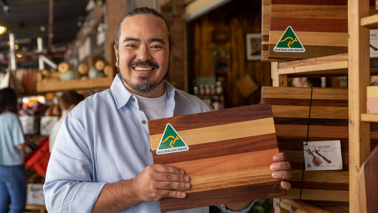 Chef Adam Liaw holds up a chopping board with a green and yellow Australian Made logo.