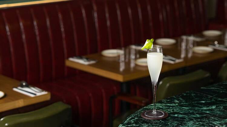 A cocktail in a champagne-style glass sits atop a green marble bar.