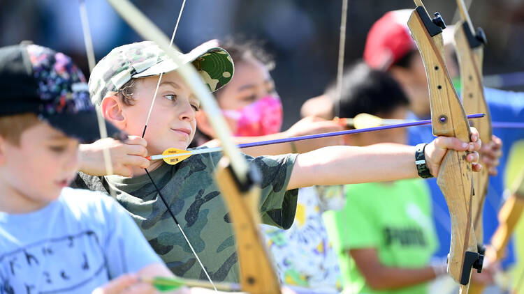 A group of children stand in a row practicing archery.