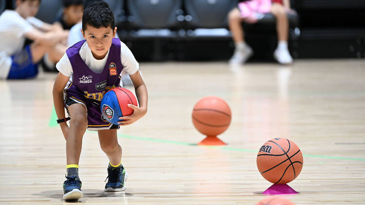 A little boy plays basketball on a court.