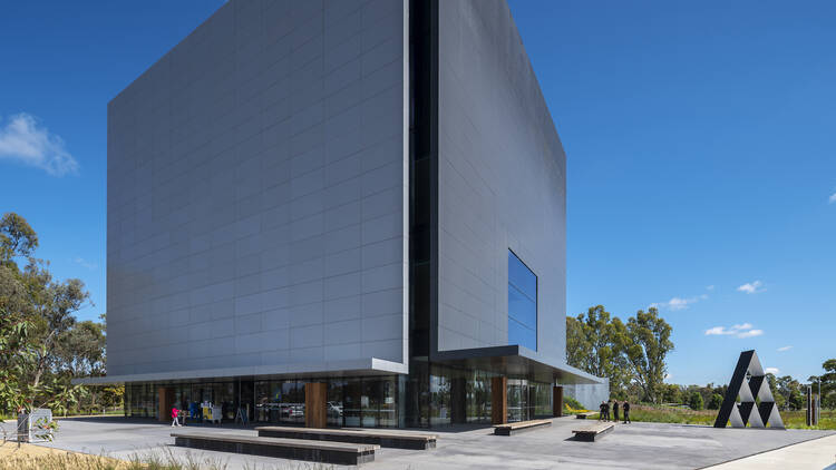 A picture of Shepparton Art Museum, a large, grey rectangular building in an open forecourt