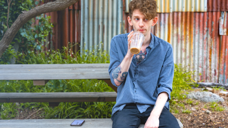 Andrew Hastings sits on a bench drinking an iced coffee