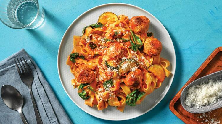 A bowl of spaghetti and meatballs on a blue tablecloth.