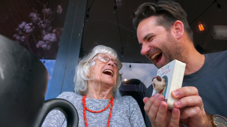 Film still from Everybody's Oma shows man joking around with his oma with a pop-up book 