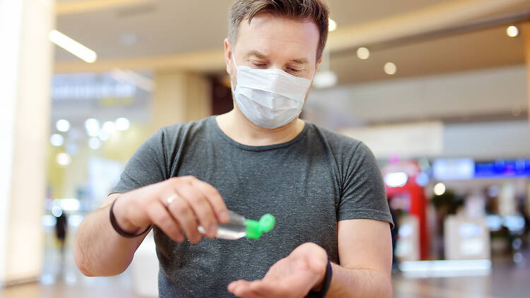 Man wearing mask puts hand sanitiser on hands