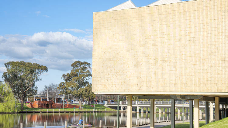 A large brick cream wall of the Benalla Art Gallery looks over a lake 