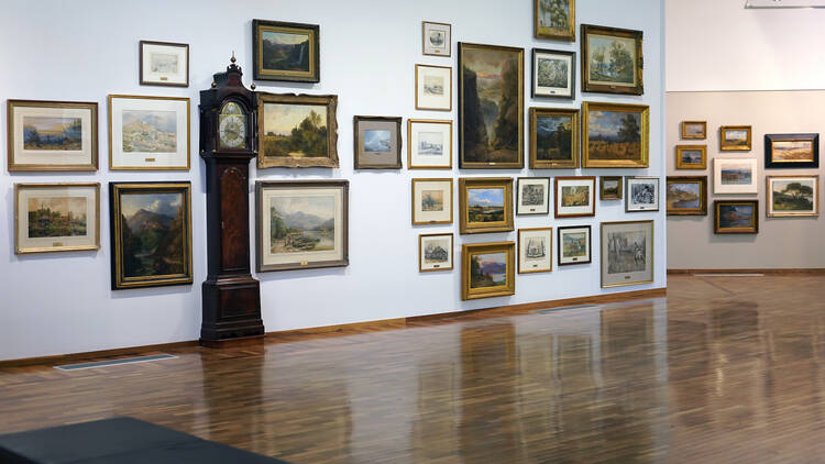 A grandfather clock sits against a gallery wall, surrounded by artworks