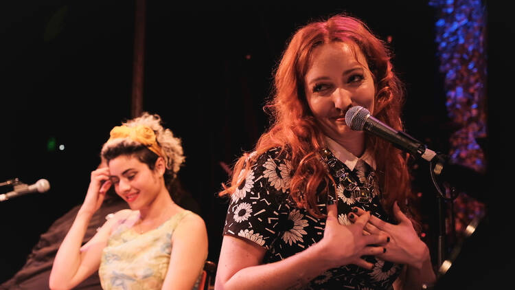 Two women look at the audience as they sit in front of microphones on stage