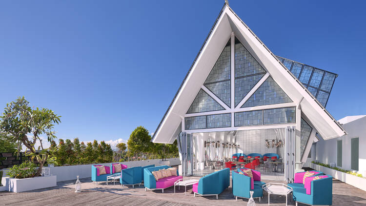 An exterior shot of a building with a high pitch roof, outdoor deck and colourful furniture.