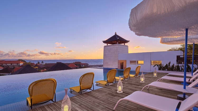 An infinity pool at sunset, with outdoor lounges and umbrellas.