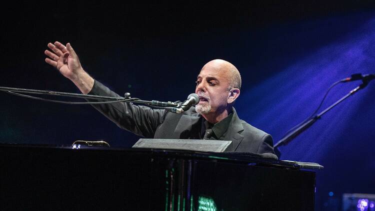 Billy Joel sitting at a piano and singing. 