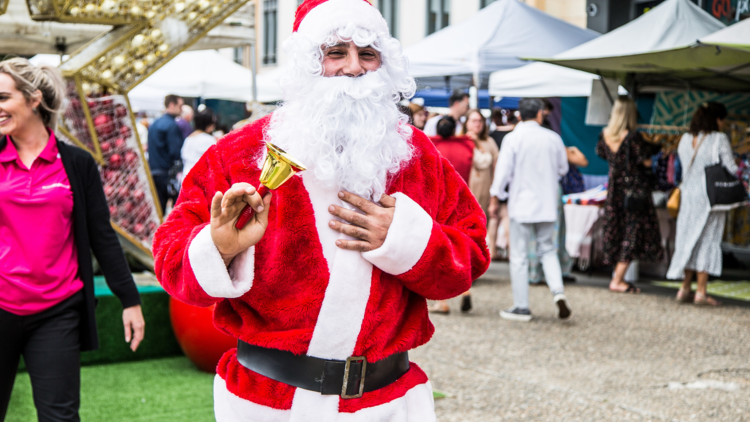 A man dressed as Santa Claus rings a gold bell