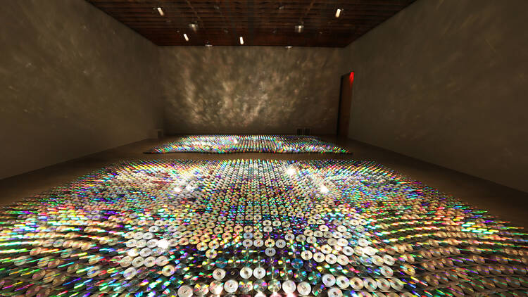A carpet of glittering compact discs extends toward the back of a huge gallery space