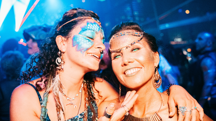 Two women smile with painted faces at a nightclub