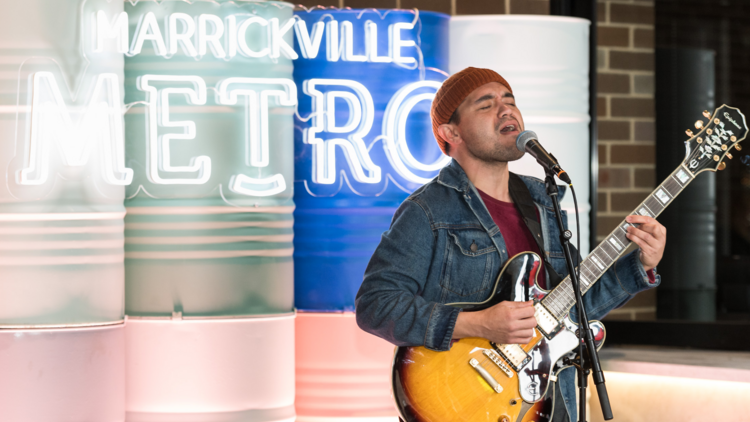 A  man sings in front of a neon wall at Marrickville Metro